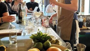Un coin bar avec un barman qui prépare des boissons, une table avec des verres et des bouteilles, et une fenêtre donnant sur un paysage.