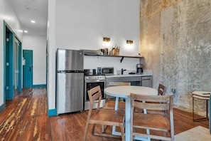 A compact kitchen with a refrigerator, stove, microwave, and coffee maker. There is a round table with chairs and a blue door in the background.