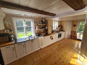Uma cozinha com piso de madeira, armários brancos, cafeteira e janela com vista para o verde.