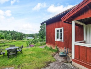A red wooden building with a white-framed window, a small porch, and a grassy yard with a table and chairs. - 5 Person Holiday Home in Mellosa (FLEN)