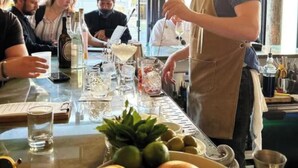 Zona de bar con un bartender preparando bebidas, una mesa con vasos y botellas, y una ventana con vistas.