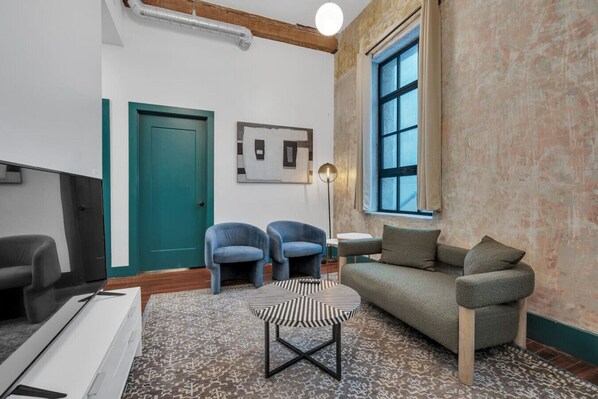 Una sala de estar moderna con una puerta azul verdosa, dos sillones azules, un sofá gris, un reposapiés estampado y un ventanal con vistas.