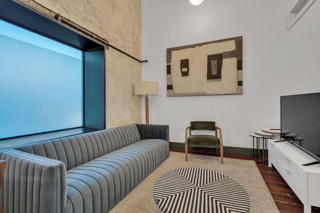 A modern living room with a sofa, a chair, a TV, and a geometric artwork on the wall.