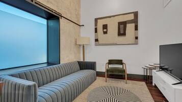 A modern living room with a sofa, a chair, a TV, and a geometric artwork on the wall.