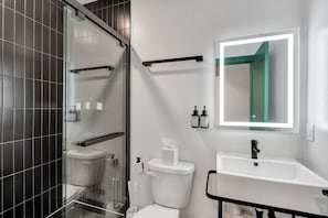 A modern bathroom with a glass shower enclosure, a white sink, and a mirror with a green accent.