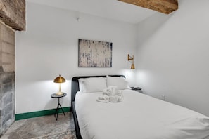 A bedroom with a bed, a lamp, a painting, and a wall-mounted light fixture.