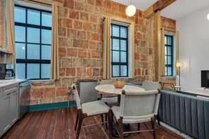 A kitchen with a brick wall, wooden floor, and a dining area with a round table and chairs.