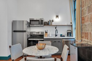 Une cuisine de taille réduite, dotée d’appareils électroménagers en acier inoxydable, d’une table ronde avec des chaises et d’un mur en briques.