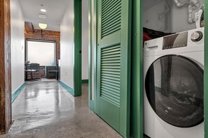 A laundry room with a washing machine, a green door, and a hallway leading to a dining area.