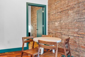 A dining area with a brick wall, a teal door, and wooden chairs around a round table.