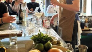 Zona de bar con un bartender preparando bebidas, una mesa con vasos y botellas, y una ventana con vistas.