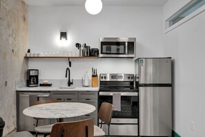A compact kitchen with a microwave, oven, and refrigerator. There is a dining table with chairs and a coffee maker.