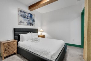 A bedroom with a bed, a nightstand, a lamp, and a painting on the wall.