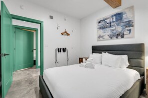 Una camera da letto con un letto, una porta verde, un'opera d'arte appesa al muro e un portascopino.