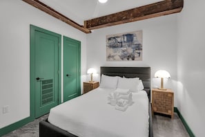A bedroom with a bed, two bedside tables with lamps, a green door, and a painting on the wall. - 3 Bedroom Apartment, French Quarter, Steps to Saenger and Canal Street (New Orleans)