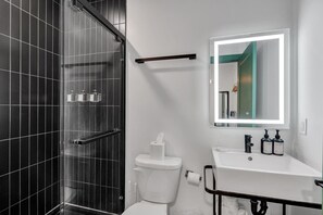 Un baño moderno con cabina de ducha de vidrio, un inodoro blanco, un lavabo con espejo y artículos de aseo.