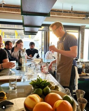 Eine Bar mit einem Barkeeper, der Getränke zubereitet, einer Speisekarte und einem Tisch mit Gläsern und Flaschen.