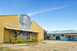 Un edificio industrial grande con un mural en la fachada y una edificación más pequeña con grafitis coloridos.
