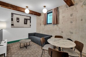 A room with a sofa, a round table, and chairs, a lamp, and a painting on the wall.