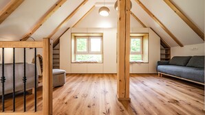 Une pièce mansardée avec des poutres en bois, un canapé, un fauteuil et deux fenêtres.
