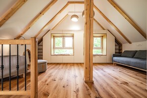 Ein Dachzimmer mit Holzbalken, einem Sofa, einem Sessel und zwei Fenstern.