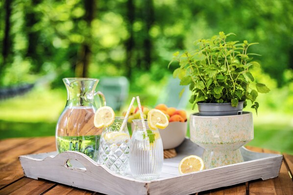 A wooden tray with a pitcher, two glasses, a bowl of fruit, and a potted plant on a wooden table.