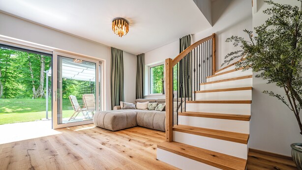Un intérieur moderne avec un escalier en bois, une grande fenêtre donnant sur un espace verdoyant et un coin salon confortable.