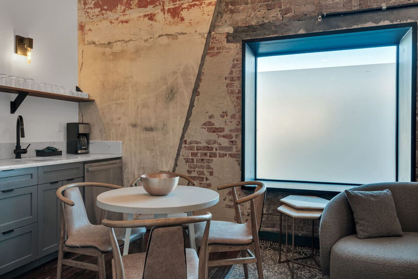 Una cocina con una mesa redonda, sillas, una cafetera y un ventanal grande.