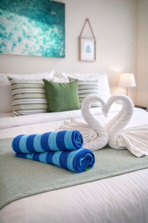A neatly made bed with striped pillows, a heart-shaped towel arrangement, and rolled towels on a textured bedspread. - King Bed Sea View Condo | 2 Resort Pools | 1min to Private Beach (Sattahip)