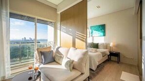 A modern hotel room with a balcony, a sofa, a bed, and a small table with a glass. - King Bed Sea View Condo | 2 Resort Pools | 1min to Private Beach (Sattahip)