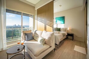 Ein modernes Hotelzimmer mit Balkon, einer Sitzecke, einem Bett und einem kleinen Tisch mit einem Glas.