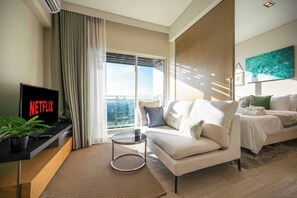 Ein modernes Wohnzimmer mit einer Couch, einem Couchtisch, einem Fernseher, der 'NETFLIX' anzeigt, und einem großen Fenster mit Vorhängen.