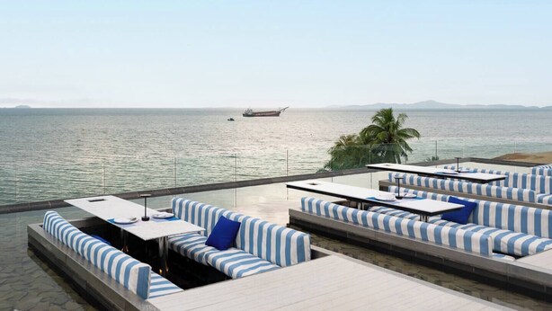 A rooftop terrace with striped seating, a view of the sea, and a ship in the distance. - King Bed Sea View Condo | 2 Resort Pools | 1min to Private Beach (Sattahip)