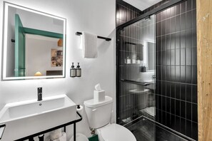 Uma casa de banho moderna com um espelho grande, uma sanita branca, uma loiça e um chuveiro com parede de vidro.