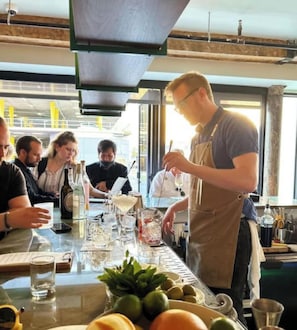 Uma área de bar com um bartender preparando bebidas, um menu e uma mesa com copos e garrafas.