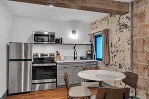 A compact kitchen with stainless steel appliances, a dining area with a round table and chairs, and a view of the outside through a window.