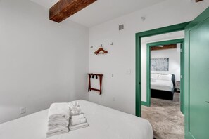 A bedroom with a bed, a wooden coat rack, a green door, and a hallway leading to another room.