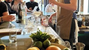 Un coin bar avec un barman qui prépare des boissons, une table avec des verres et des bouteilles, et une fenêtre donnant sur un paysage.