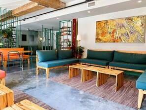 A modern living room with green sofas, wooden coffee tables, and a large abstract painting on the wall.
