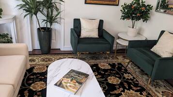 Ein Wohnzimmer mit Sofa, Sesseln, Couchtisch, Zimmerpflanze, Gemälde und Spiegel.