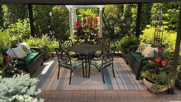 Ein überdachter Patio-Bereich mit Tisch und Stühlen, umgeben von Blumentöpfen und einer Sitzecke.