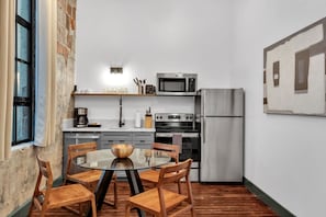 Cuina compacta amb taula de dinar, cadires, nevera, microones, forn i una finestra.