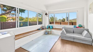 A bright room with large windows, a grey sofa, a small table, and a play area with toys. - Peaceful Single-Level Modern Luxury with Private Yard and AC in La Jolla (San Diego)