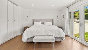 A modern bedroom with a large bed, a bench, and a view through glass doors. - Peaceful Single-Level Modern Luxury with Private Yard and AC in La Jolla (San Diego)