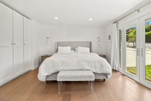 Ein modernes Schlafzimmer mit einem großen Bett, einer Bank und Blick durch Glastüren.