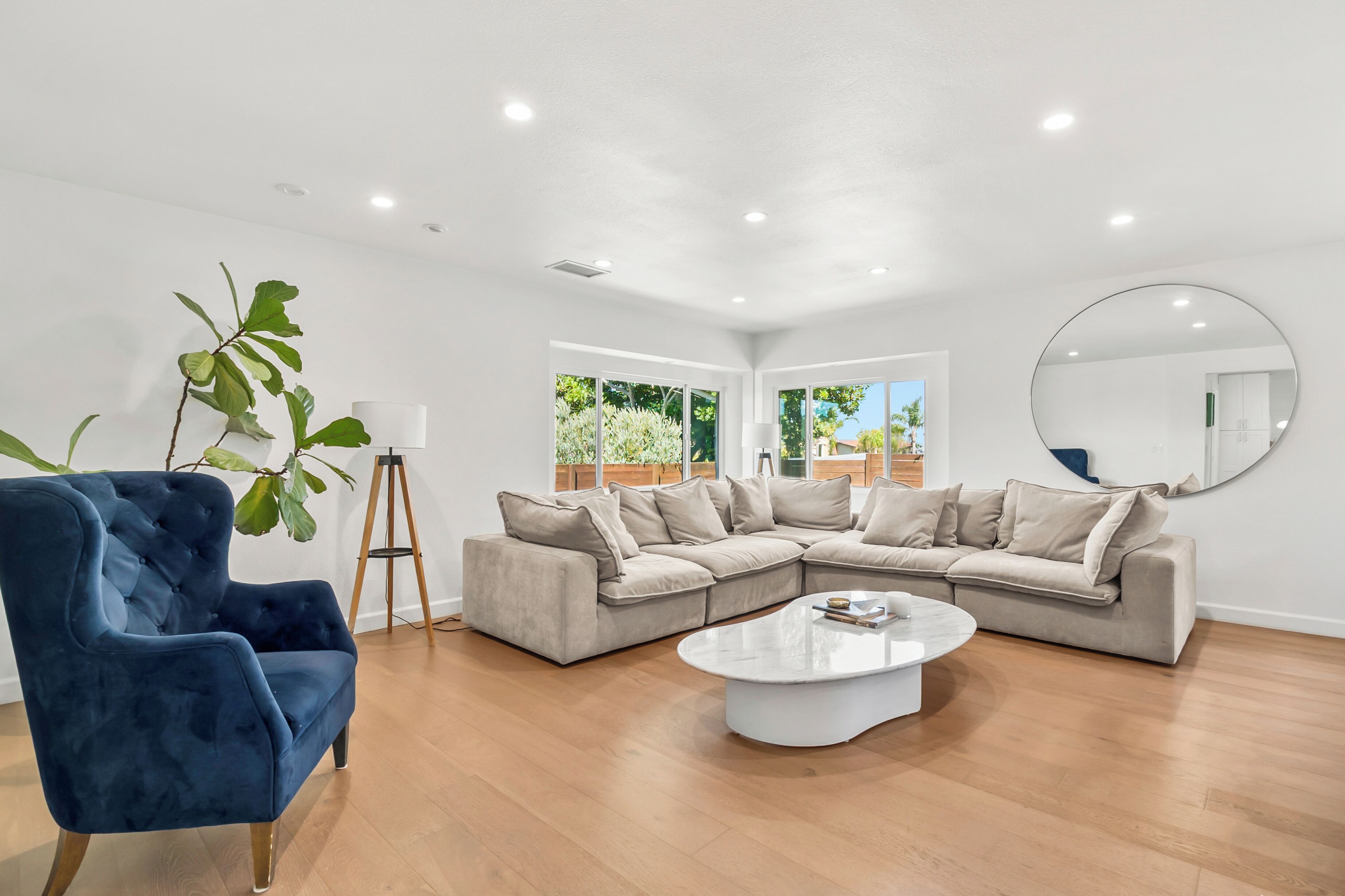 A modern living room with a sectional sofa, a blue armchair, a round coffee table, and a large mirror on the wall.