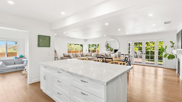 A spacious kitchen with a large island, a dining area with a sofa and chairs, and a view through glass doors to the outdoors. - Peaceful Single-Level Modern Luxury with Private Yard and AC in La Jolla (San Diego)