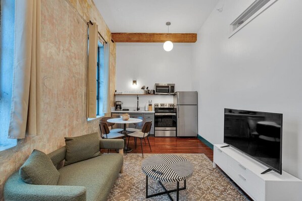 Espaço compacto com sofá, mesa de jantar, cadeiras, televisão, cozinha equipada e uma janela grande.
