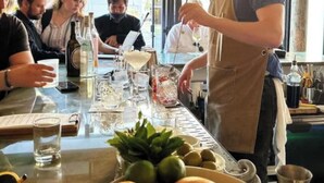 Zona de bar con un bartender preparando bebidas, una mesa con vasos y botellas, y una ventana con vistas.