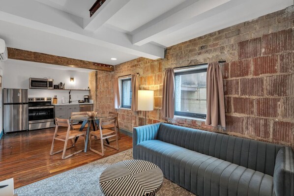 Una cucina moderna con elettrodomestici in acciaio inossidabile, un'area pranzo con tavolo e sedie in legno, un divano blu e una parete in mattoni.